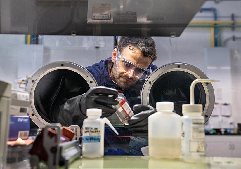 A researcher uses a glove box to hold a glass jar.